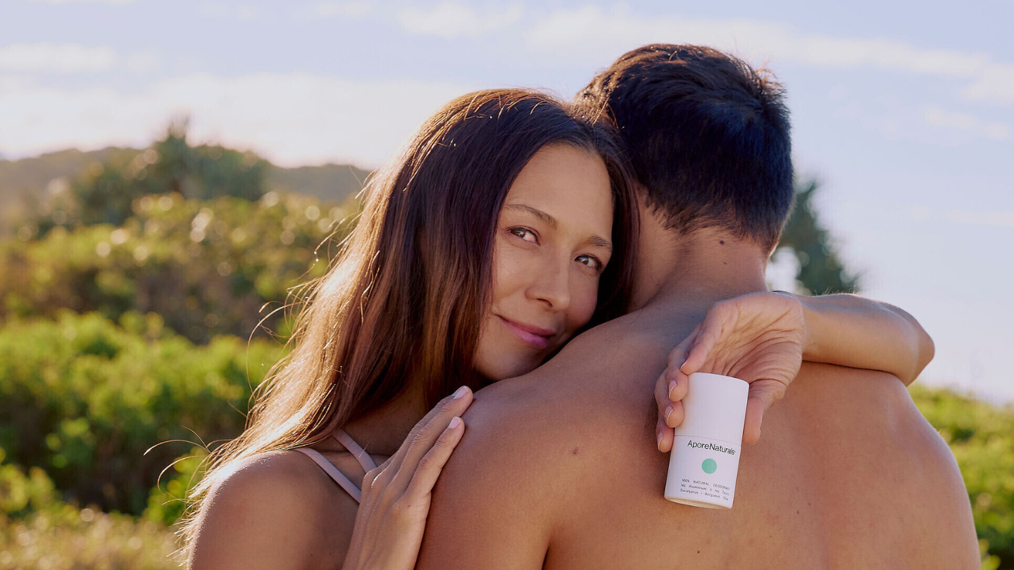 Woman embracing a man outdoors with AporeNaturals deodorant in her hand